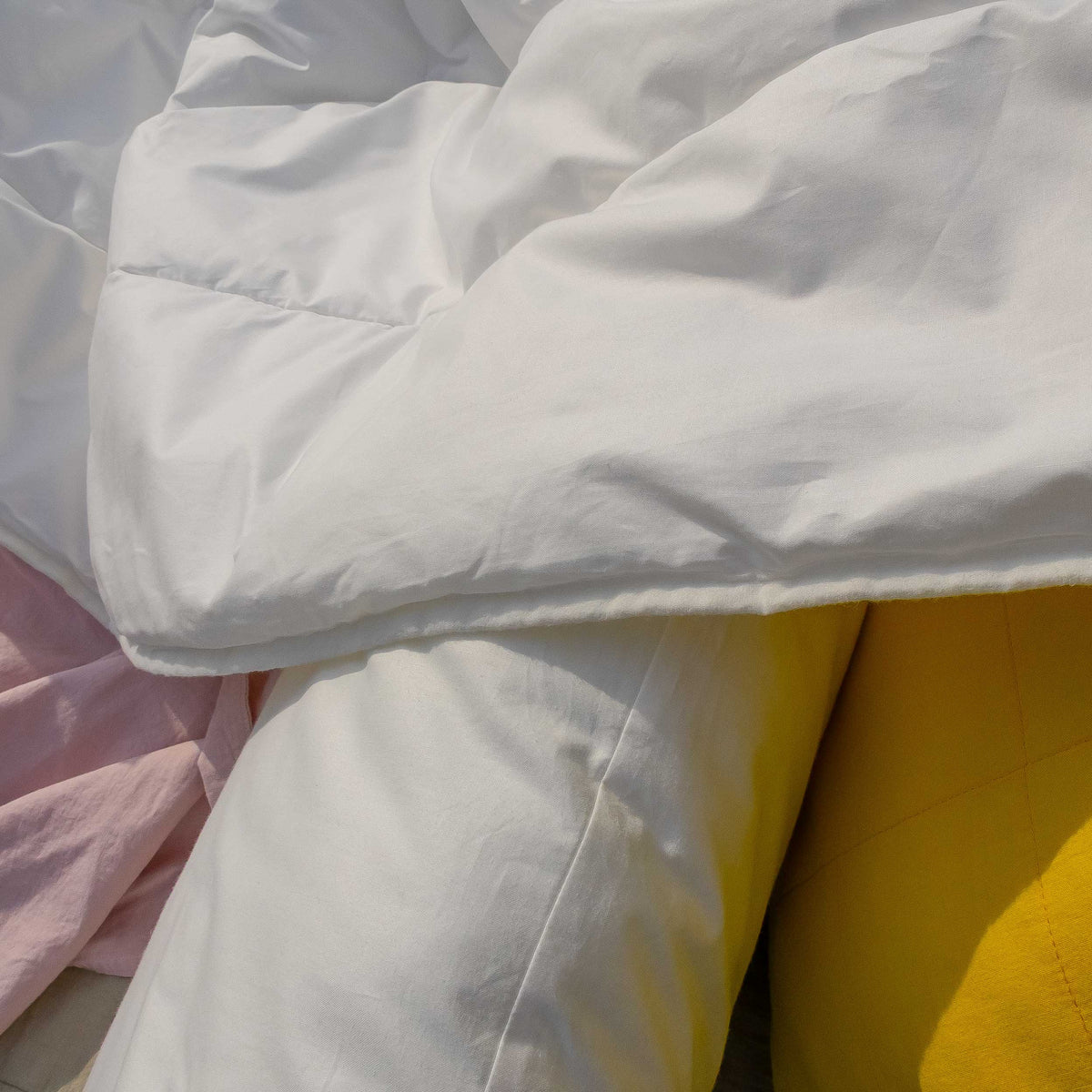 Nahaufnahme der weißen, leicht zerknitterten Prima Sommerdecke mit gelbem und rosa Bettbezug im Hintergrund