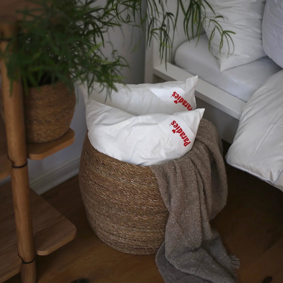 Nahaufnahme eines geflochtenen Korbs mit zwei weißen Kissen mit roter Aufschrift und einer braunen Decke daneben