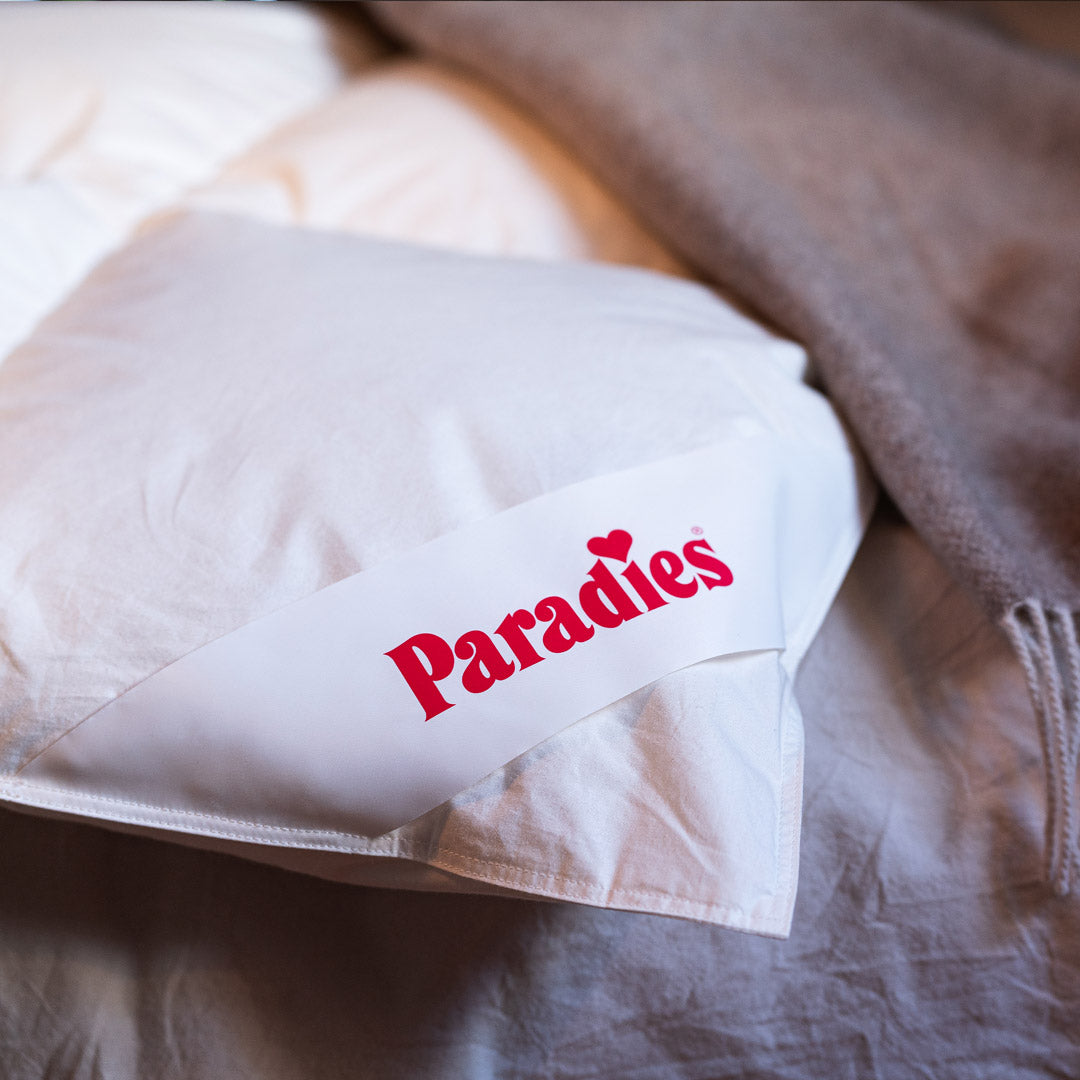 Nahaufnahme eines weißen Kissens mit einem weißen Etikett, auf dem in roter Schrift 'Paradies' steht