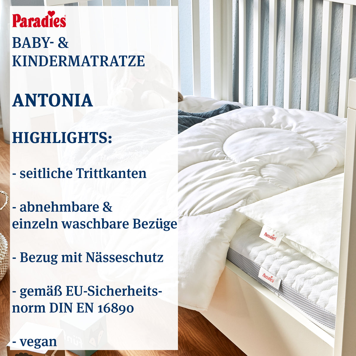 Babymatratze mit abnehmbarem, weißem Bezug und sichtbarer grauer Matratzenkante in einem weißen Gitterbett auf Holzboden