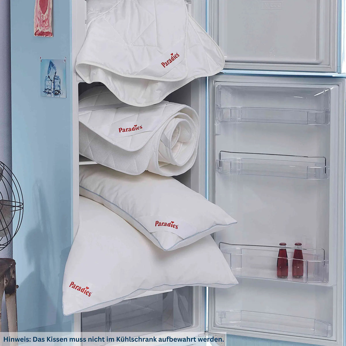 Offener Kühlschrank mit mehreren weißen Kissen und Decken mit rotem Paradies-Logo sowie einem Hinweistext am unteren Bildrand