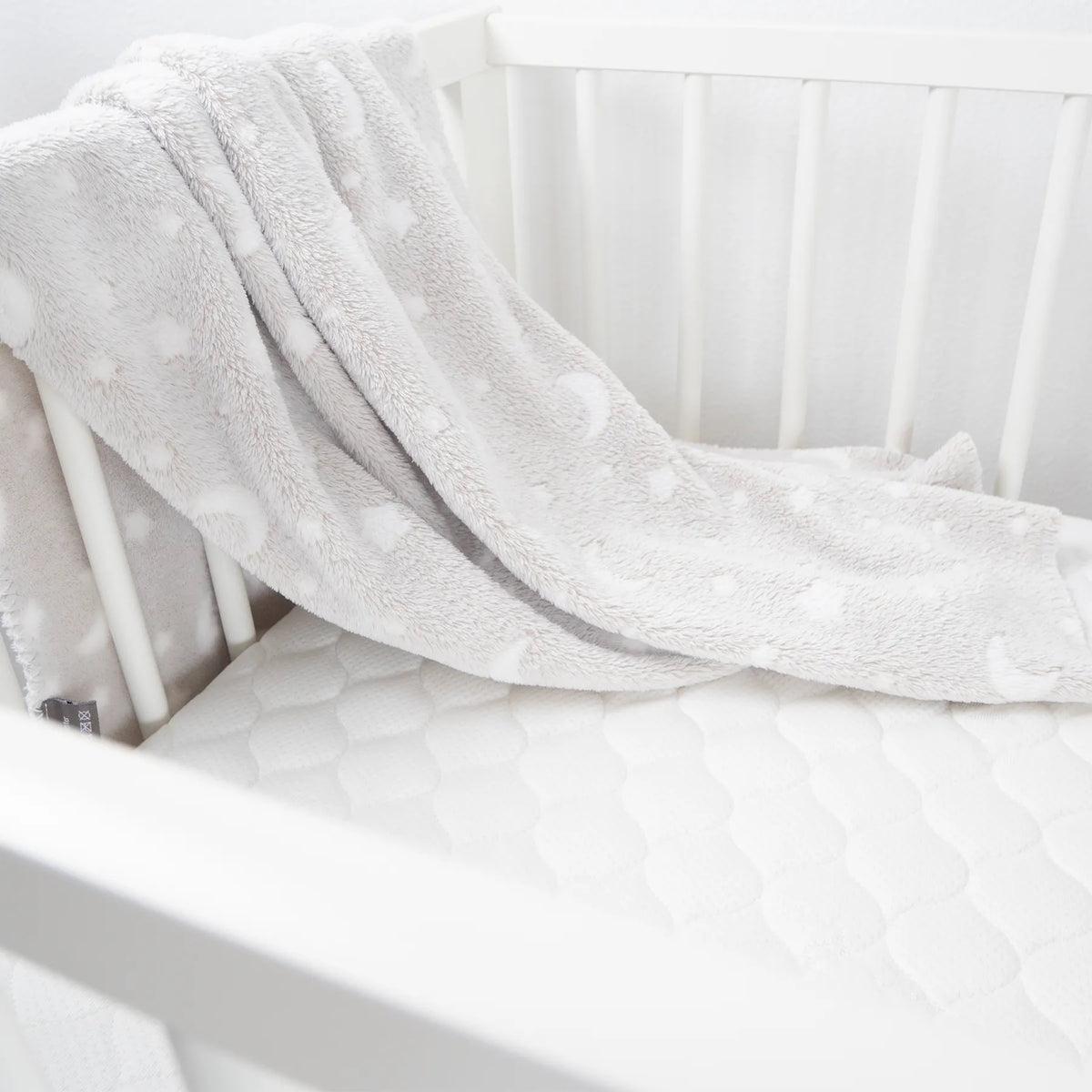 Weiche Decke mit Stern- und Mondsymbolen liegt in weißem Babybett mit Gitterstäben