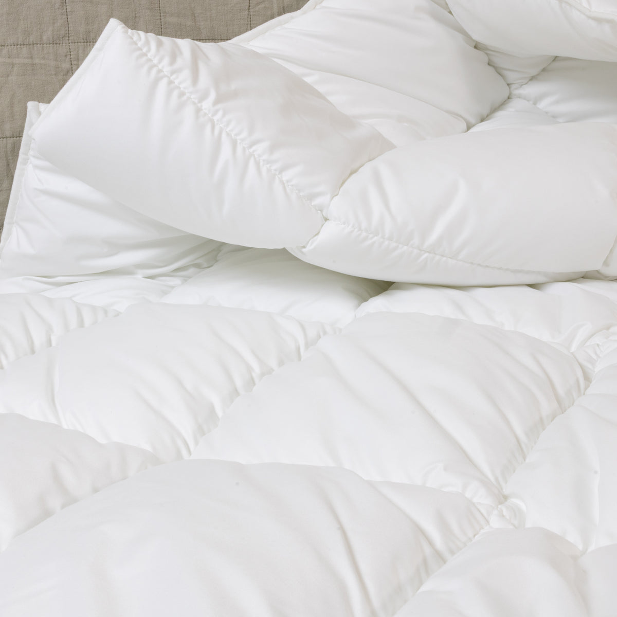 Bett mit weißer Steppdecke, mehreren weißen und einem rosafarbenen Kissen mit roter Aufschrift sowie einem Blumenstrauß in Vase auf Nachttisch