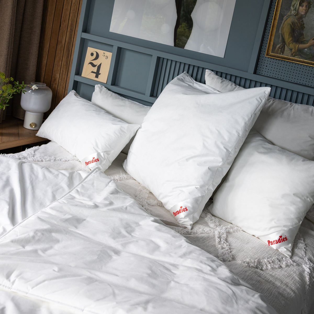 Drei weiße Softy Antiallergo Kissen mit rotem Paradies-Logo auf einem Bett mit Antiallergo Bettdecke und blauem Kopfteil