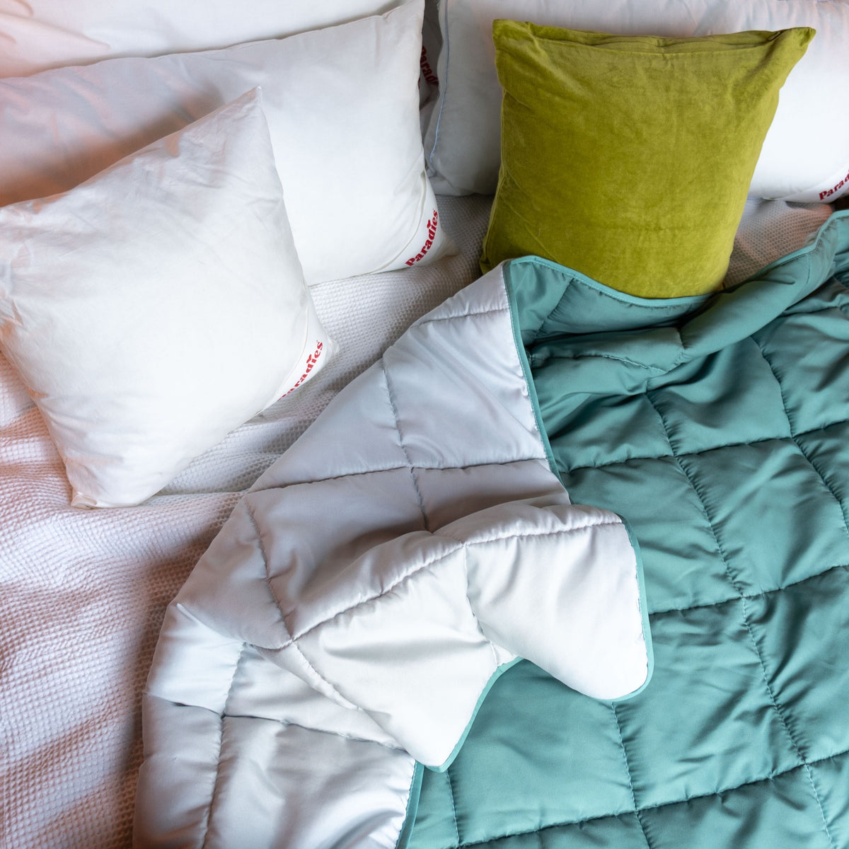 Bett mit weißen Kissen und grünem Kissen sowie einer zweifarbigen Steppdecke in Grün & Grau