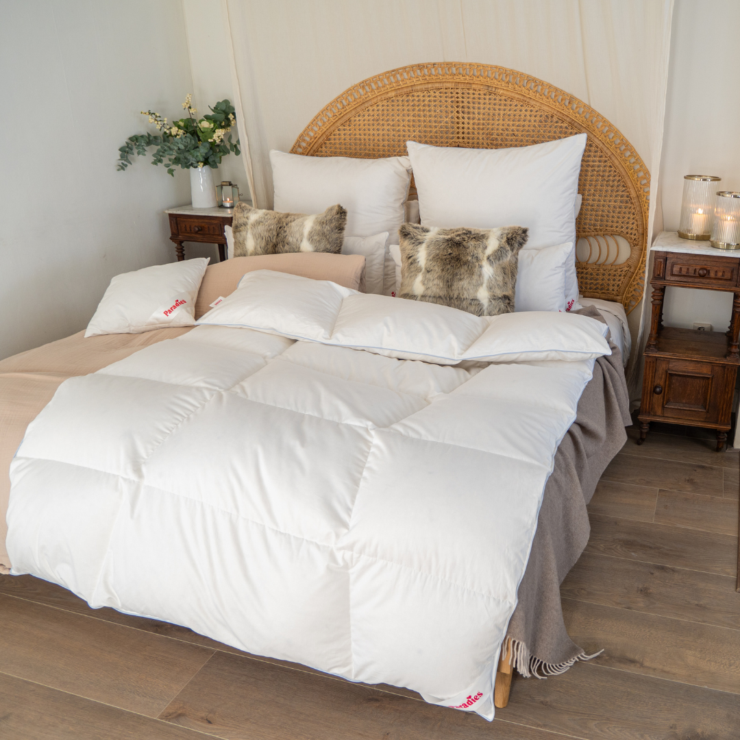 Winterbettdecke mit Gänsedaunenfüllung auf einem Bett mit Rattankopfteil, dekoriert mit weißen und Fellkissen
